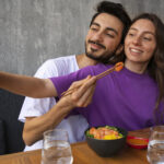 Pareja joven compartiendo comida y tomando una selfie, ejemplo de amor inteligente y momentos felices en pareja.