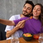 Pareja joven compartiendo comida y tomando una selfie, ejemplo de amor inteligente y momentos felices en pareja.
