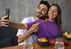 Pareja joven compartiendo comida y tomando una selfie, ejemplo de amor inteligente y momentos felices en pareja.