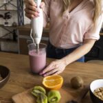 Mujer preparando jugos medicinales caseros con frutas frescas en la cocina